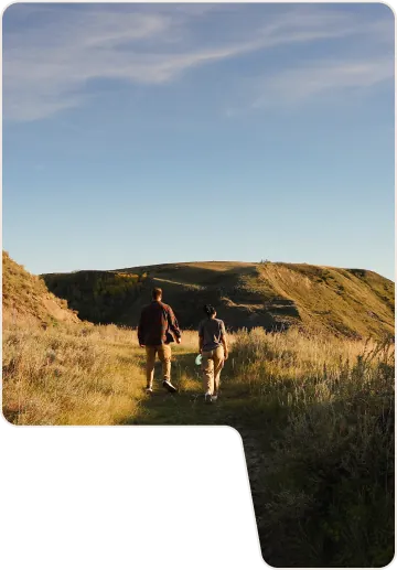 Hero Image - two people walking over grassy dunes